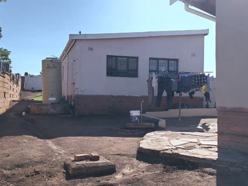 Rear exterior view of the property featuring a paved patio area, brick foundation, and a water storage tank.