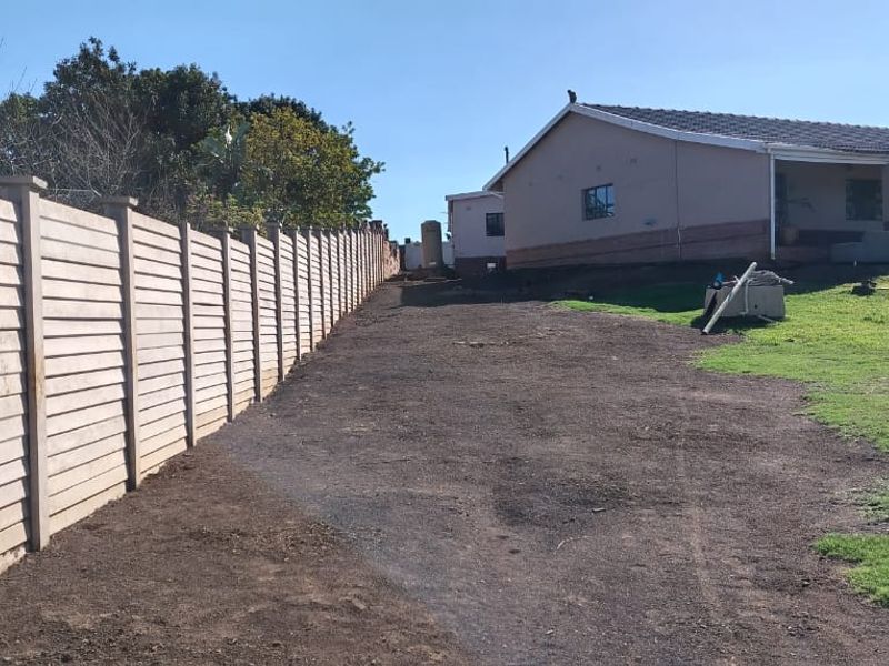 A view of the rear yard featuring a long precast concrete boundary wall, an unlandscaped dirt area, and the rear elevation of the house.