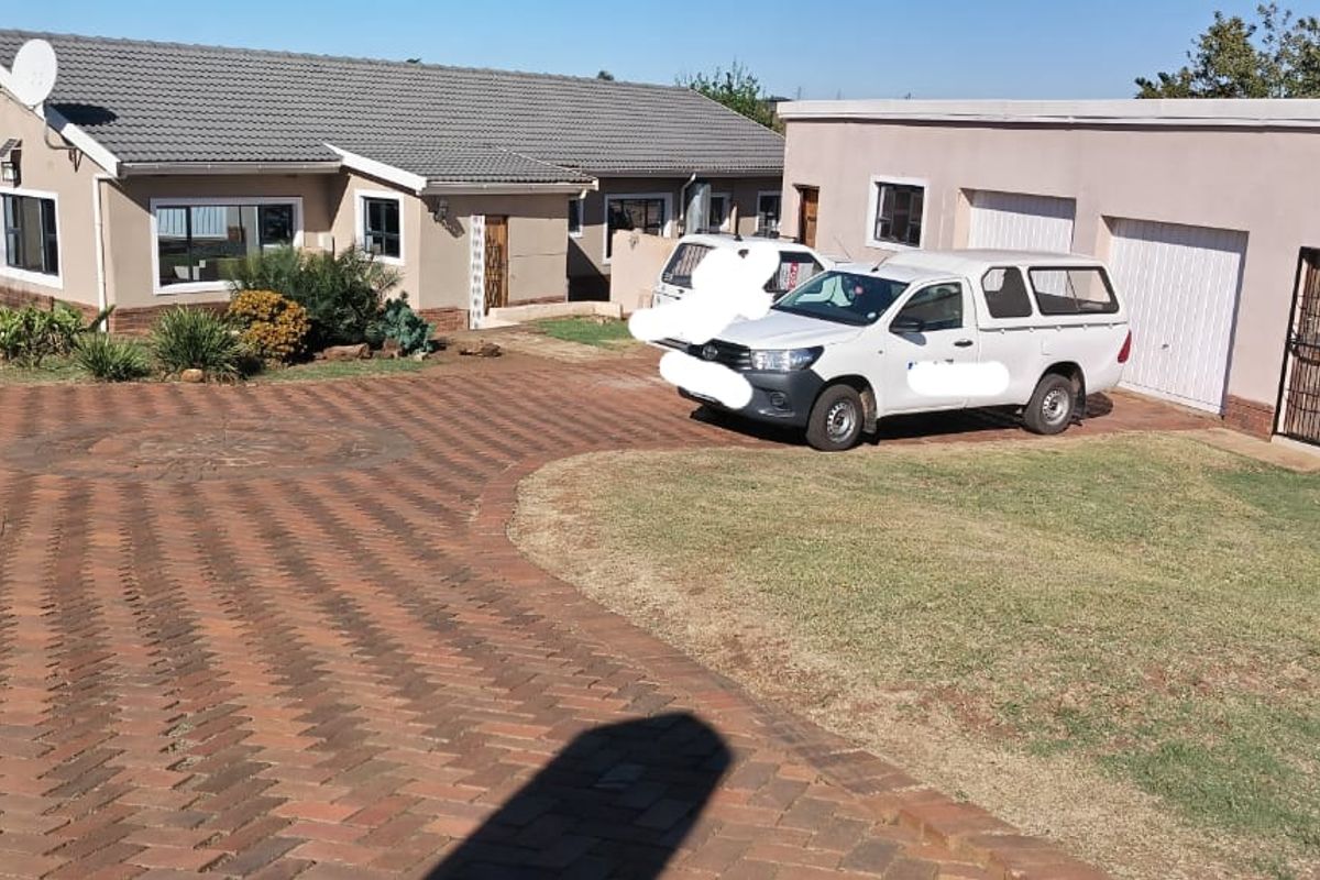 Front exterior view of a single-story house featuring a tiled roof, brick chimney, paved driveway, and a double garage with a surrounding lawn.