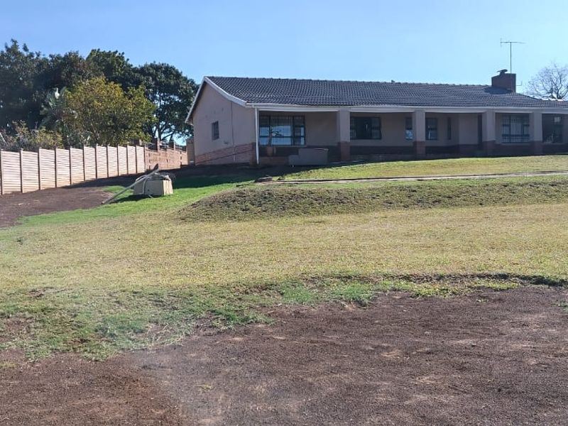 Rear view of the house featuring a covered patio, tiled roof, and a large garden area enclosed by precast concrete boundary walls.