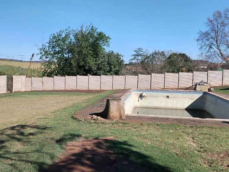 Outdoor pool area featuring a large swimming pool, perimeter fencing, and expansive lawn space with rural views.