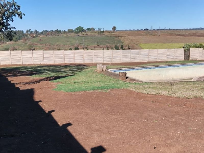 Spacious backyard featuring a large swimming pool enclosed by a precast concrete boundary wall, offering potential for landscaping and outdoor renovation.