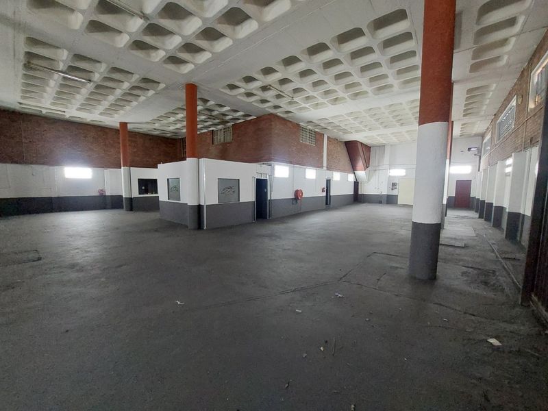 Spacious open-plan commercial area featuring a distinctive waffle slab ceiling, exposed brick walls, and durable concrete flooring, suitable for various business applications.