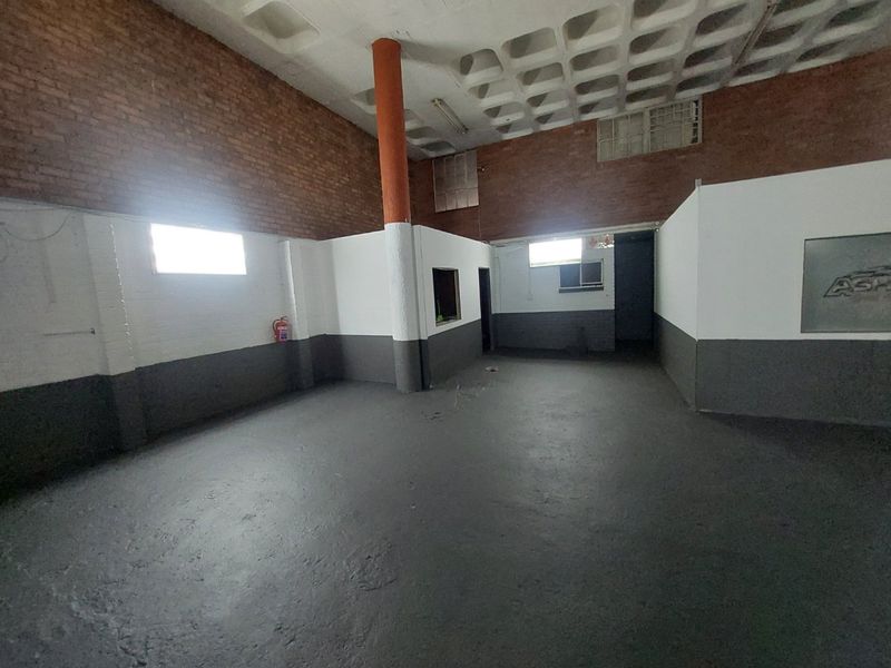 An open-plan commercial utility space featuring exposed brickwork, a waffle slab ceiling, and painted concrete flooring.