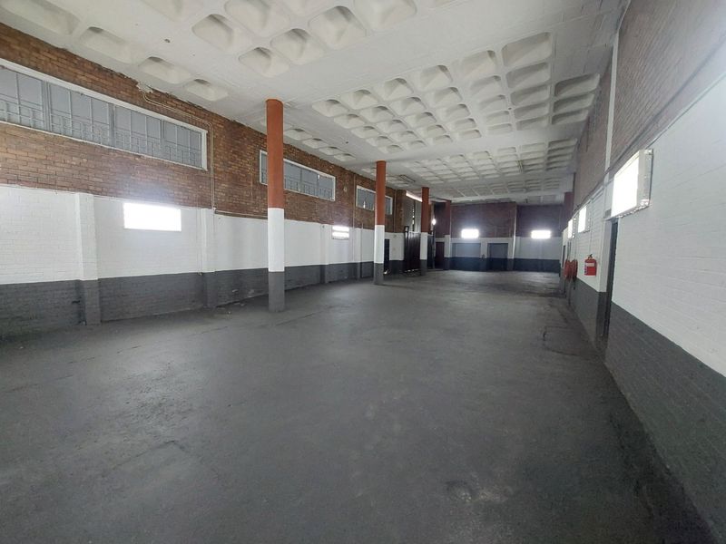 Spacious commercial utility area featuring a distinctive waffle slab ceiling, exposed brickwork, and durable concrete flooring, suitable for storage or industrial use.