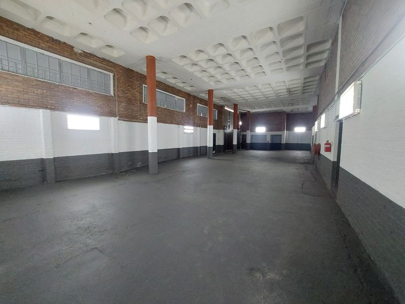 A spacious, empty commercial utility or warehouse area featuring exposed brick walls, structural columns, and a distinctive waffle slab ceiling.