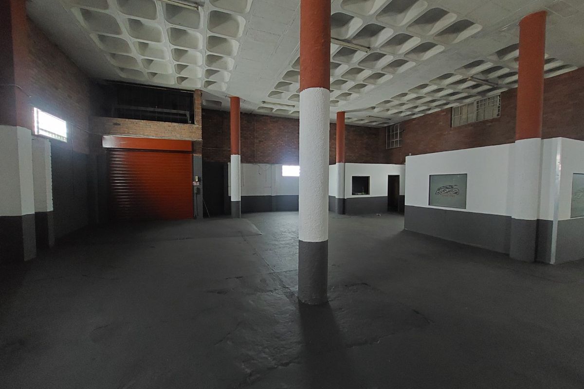 Spacious commercial utility area featuring a distinctive waffle slab ceiling, exposed brickwork, concrete columns, and a secure roller shutter door.