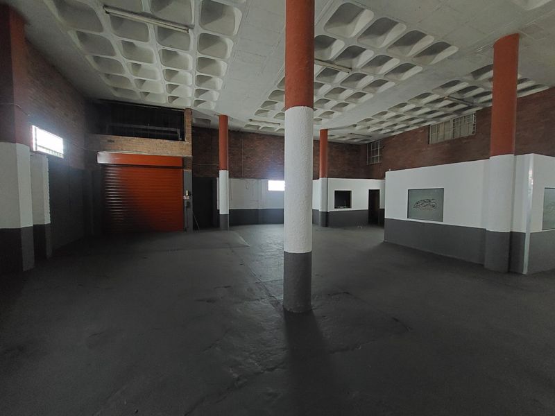 Spacious commercial utility area featuring a distinctive waffle slab ceiling, exposed brickwork, concrete columns, and a secure roller shutter door.