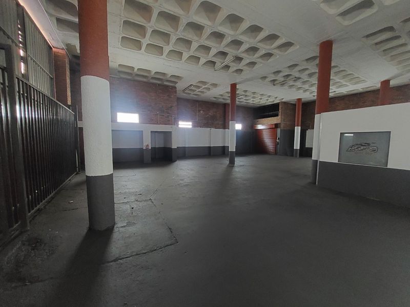 Spacious commercial utility area featuring exposed brick walls, structural columns, a waffle slab ceiling, and a secure roller shutter door entrance.