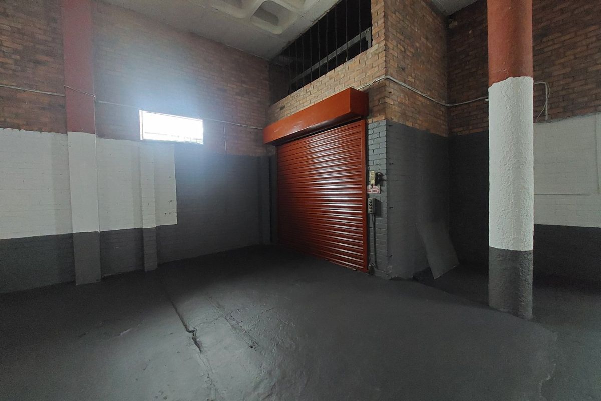 Spacious commercial garage or warehouse area featuring exposed brick walls, concrete columns, a high waffle slab ceiling, and a secure roller shutter door.