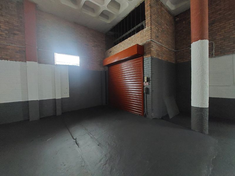 Spacious commercial garage or warehouse area featuring exposed brick walls, concrete columns, a high waffle slab ceiling, and a secure roller shutter door.