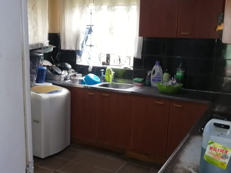 A functional kitchen featuring dark laminate cabinetry, a stainless steel sink, tiled backsplash, and tiled flooring, requiring cosmetic updates to modernize the space.