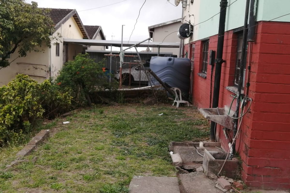 Rear exterior area featuring a concrete utility sink, water storage tank, and basic garden space with visible wear to the building facade.