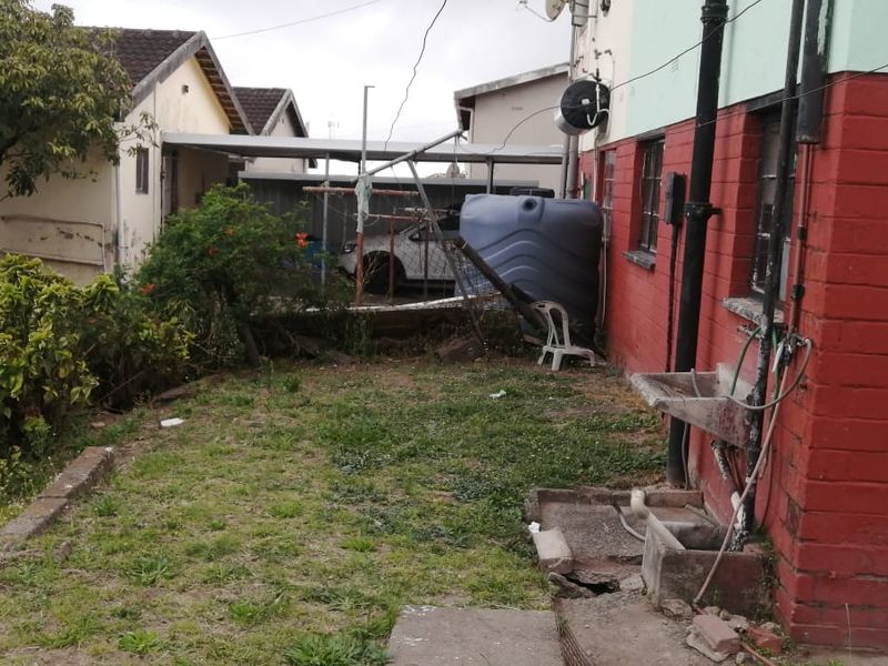 Rear exterior area featuring a concrete utility sink, water storage tank, and basic garden space with visible wear to the building facade.