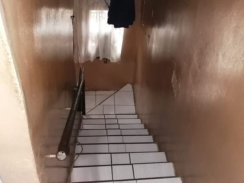 A narrow interior staircase featuring white tiled steps and a simple metal handrail, leading to a lower level.