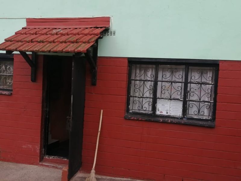 Exterior view of a residential building featuring a red and green painted brick facade with a small tiled entrance awning and security window bars.