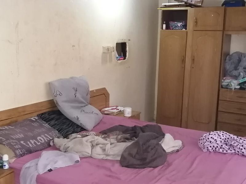 A bedroom featuring a built-in wooden wardrobe, showing signs of wear and significant wall damage requiring repair and cosmetic attention.