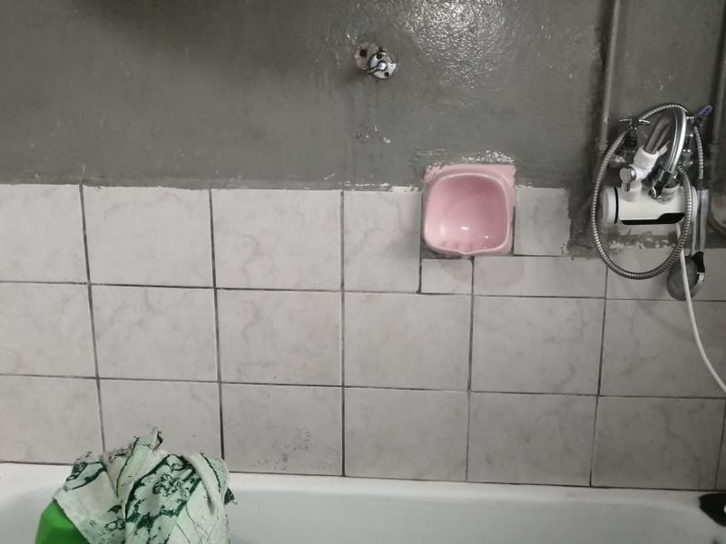 A bathroom area featuring a bathtub with wall tiling, requiring significant renovation to address unfinished wall surfaces and exposed plumbing fixtures.