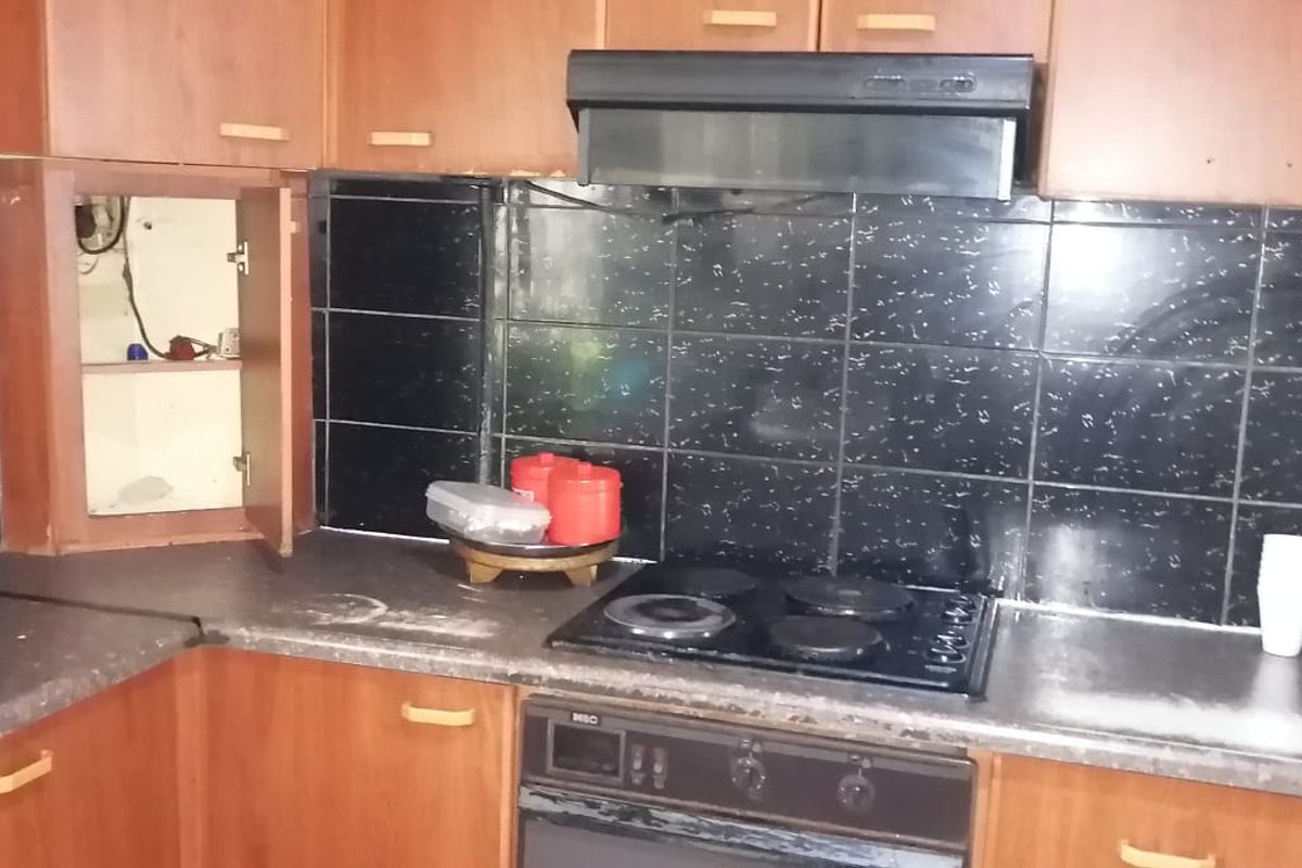 A dated kitchen featuring wood-tone cabinetry, black tiled backsplash, and integrated cooking appliances, currently requiring maintenance and cosmetic updates.