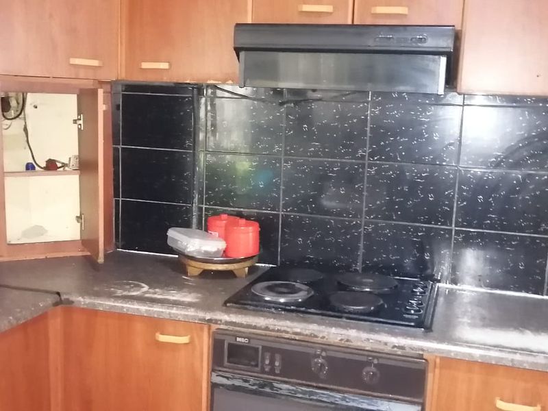 A dated kitchen featuring wood-tone cabinetry, black tiled backsplash, and integrated cooking appliances, currently requiring maintenance and cosmetic updates.