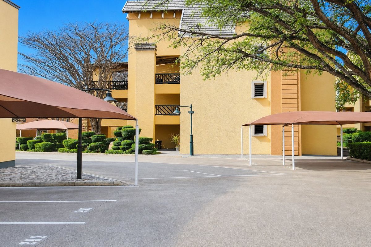 Exterior view of the apartment complex featuring paved parking areas with shade ports and well-maintained landscaped grounds.