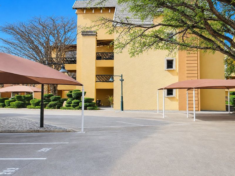 Exterior view of the apartment complex featuring paved parking areas with shade ports and well-maintained landscaped grounds.