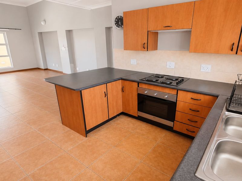 Open-plan kitchen and living area featuring wood-finish cabinetry, electric cooking appliances, tiled flooring, and direct access to a balcony.