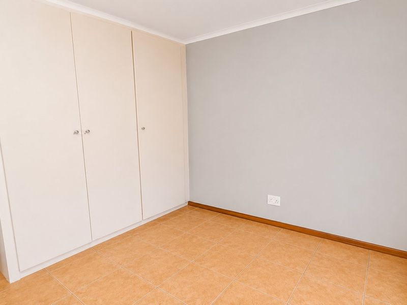 A clean, empty bedroom featuring neutral walls, tiled flooring, and ample built-in cupboard storage with venetian blinds on the window.