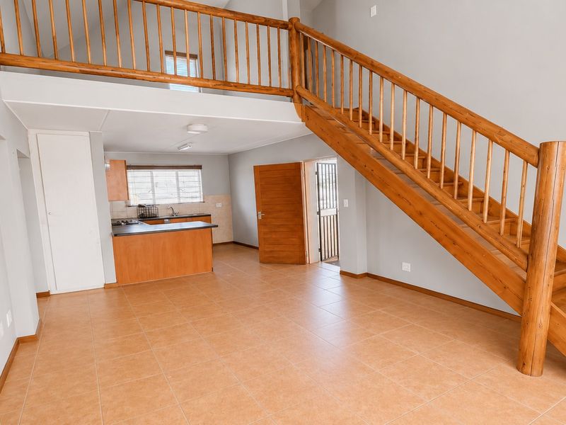 Spacious open-plan living area featuring tiled floors, a wooden staircase with balustrade, and a functional kitchen with built-in cabinetry.