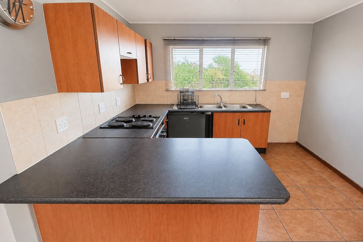 A functional kitchen featuring laminate cabinetry, dark countertops, an electric hob, and a double bowl sink with tiled backsplash and flooring.