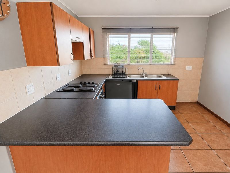 A functional kitchen featuring laminate cabinetry, dark countertops, an electric hob, and a double bowl sink with tiled backsplash and flooring.