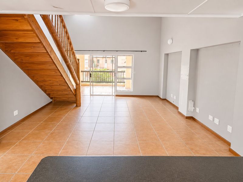 Spacious open-plan living area featuring tiled floors, a wooden staircase, and direct access to a balcony through sliding glass doors.