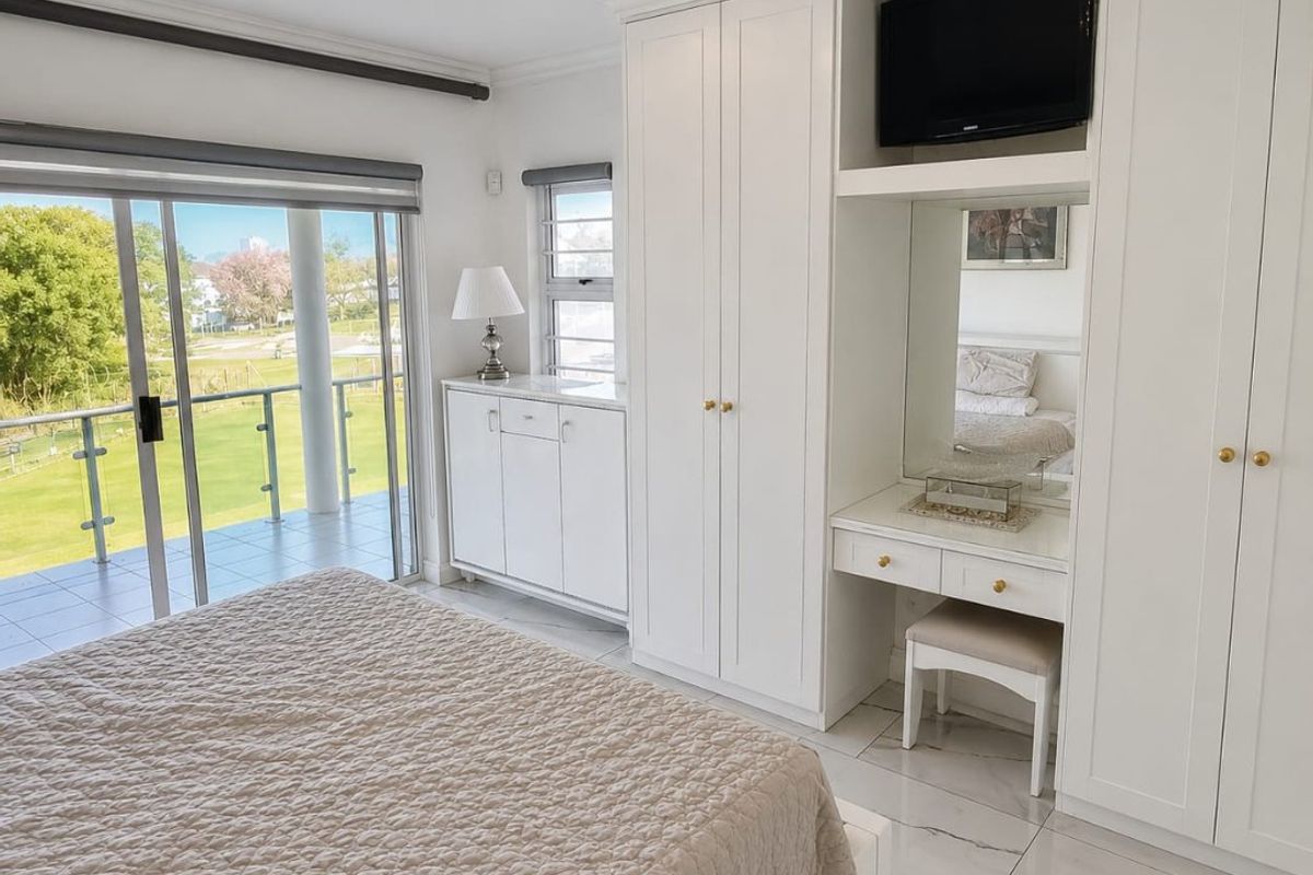 Spacious bedroom featuring built-in cabinetry, a vanity station, marble-look flooring, and sliding glass doors opening onto a private balcony with scenic views.