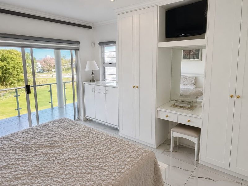 Spacious bedroom featuring built-in cabinetry, a vanity station, marble-look flooring, and sliding glass doors opening onto a private balcony with scenic views.