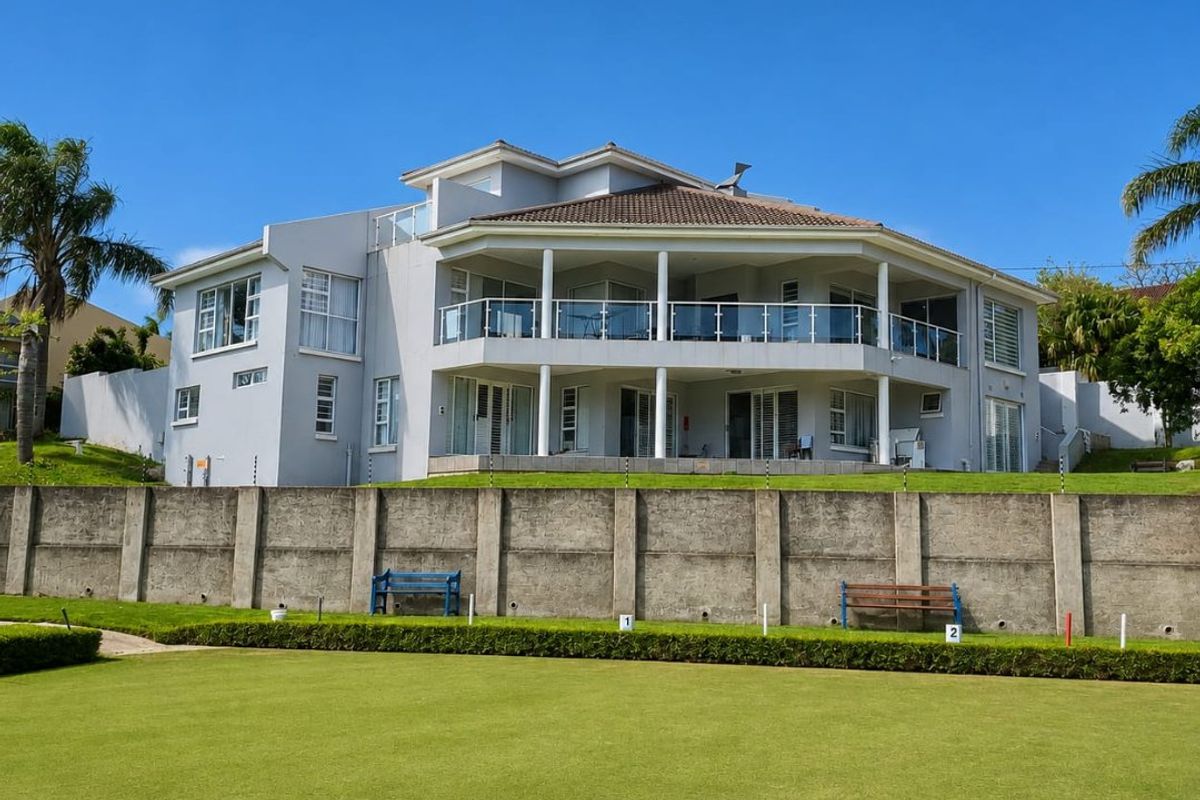 Rear view of a multi-story residential property featuring expansive balconies with glass balustrades, overlooking a manicured lawn and concrete boundary wall.