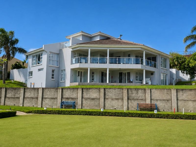 Rear view of a multi-story residential property featuring expansive balconies with glass balustrades, overlooking a manicured lawn and concrete boundary wall.
