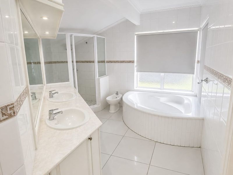 A bright, spacious bathroom featuring a double vanity, a built-in bathtub, a separate shower enclosure, and a bidet with neutral white tiling throughout.