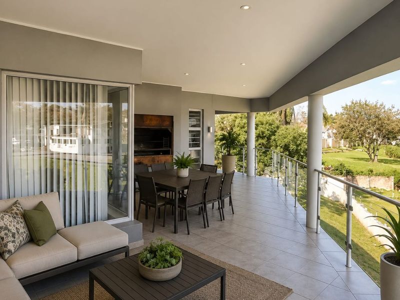 Spacious covered balcony featuring tiled flooring, a built-in braai, and a modern glass balustrade overlooking the garden.