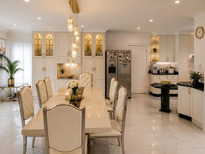 A bright and elegant open-plan dining and kitchen area featuring high-end cabinetry, polished marble-look flooring, and sophisticated pendant lighting.