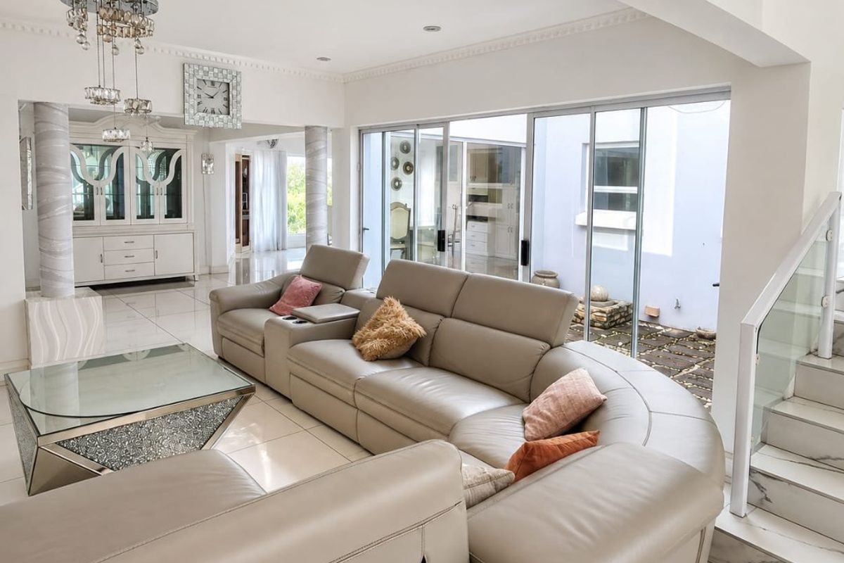 Spacious living area featuring polished tile flooring, modern glass staircase balustrade, and large sliding doors providing seamless access to the outdoor courtyard.