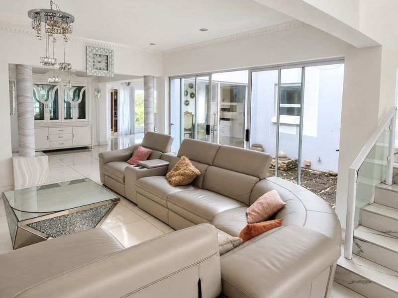 Spacious living area featuring polished tile flooring, modern glass staircase balustrade, and large sliding doors providing seamless access to the outdoor courtyard.