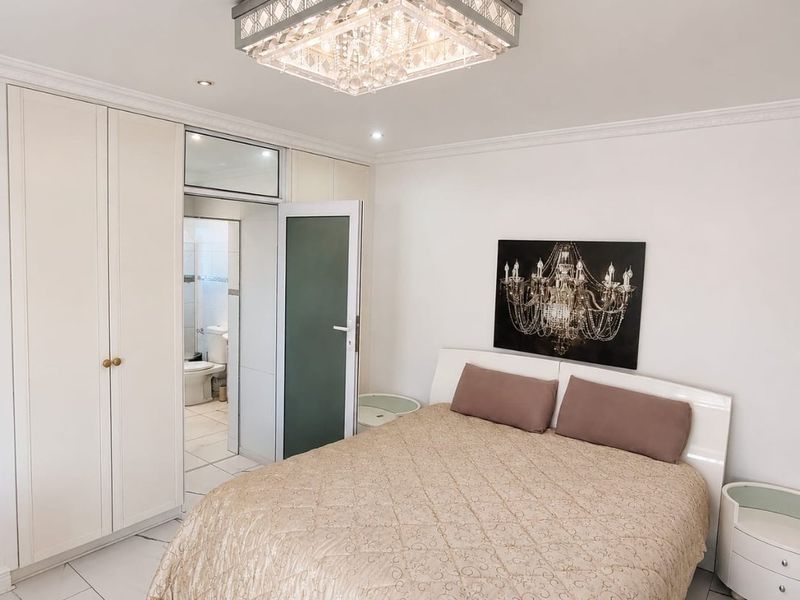 A well-maintained bedroom featuring built-in cupboards, modern tiled flooring, a decorative ceiling light, and direct access to an en-suite bathroom.