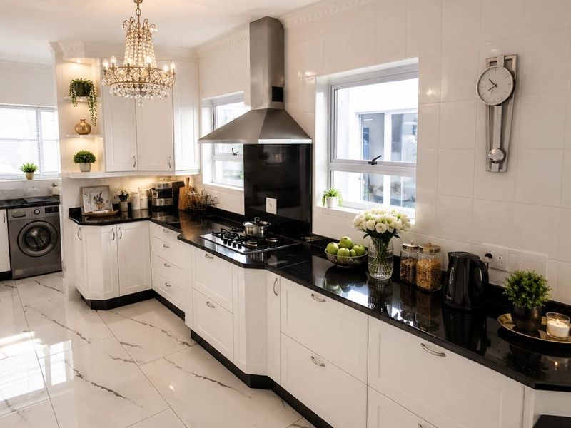 Modern kitchen featuring white cabinetry, black granite countertops, gas hob, stainless steel extractor, and elegant marble-look floor tiles with integrated laundry area.