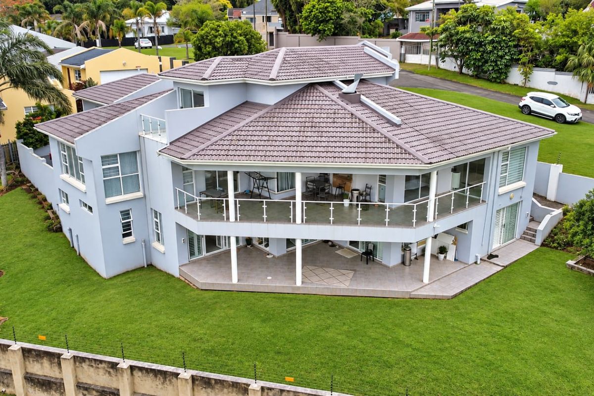 Aerial view of a multi-level residential property featuring a tiled roof, expansive covered balconies with glass balustrades, and a well-maintained garden with perimeter security.