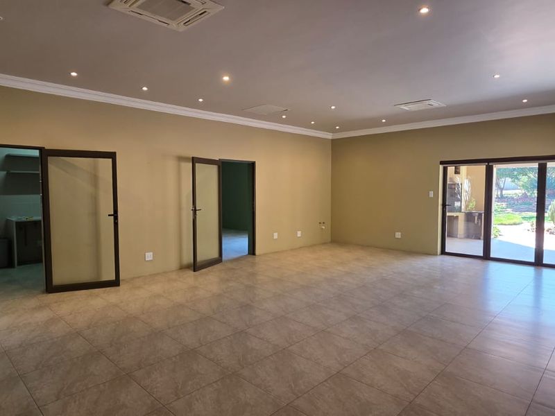 Spacious, open-plan living area featuring neutral tiled flooring, recessed lighting, ducted air conditioning, and large sliding glass doors leading to the outdoor area.