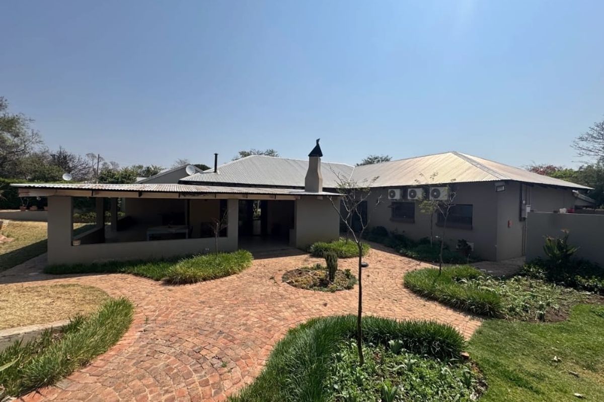 Rear view of the property featuring a covered patio, brick-paved courtyard, and well-maintained landscaped garden areas.