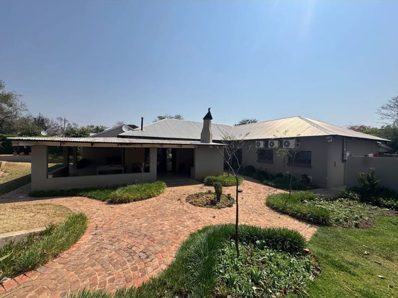 Rear view of the property featuring a covered patio, brick-paved courtyard, and well-maintained landscaped garden areas.