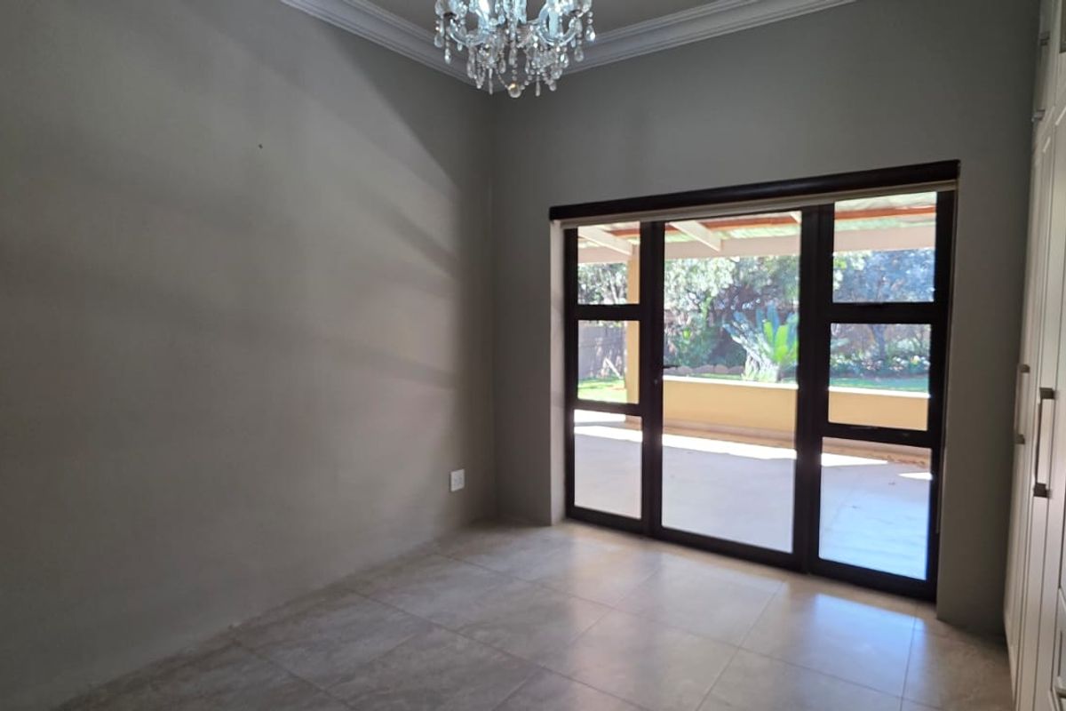 A bright, empty bedroom featuring built-in cupboards, tiled flooring, crown molding, and a sliding glass door providing access to the outdoor patio area.