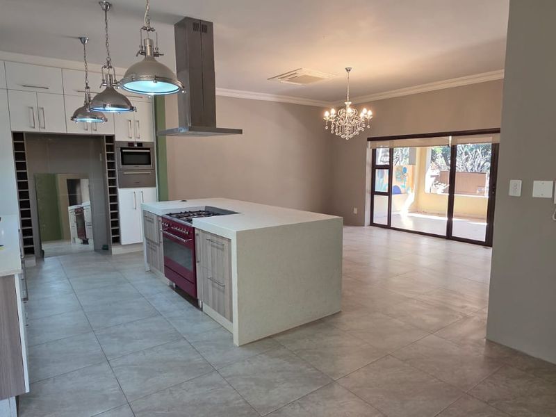 Spacious open-plan kitchen and living area featuring a large central island, modern cabinetry, stone countertops, and direct access to an outdoor patio.