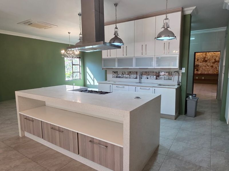 Modern kitchen featuring a large central island with stone countertops, built-in cabinetry, gas cooktop, and stainless steel extractor hood, finished with tiled flooring.